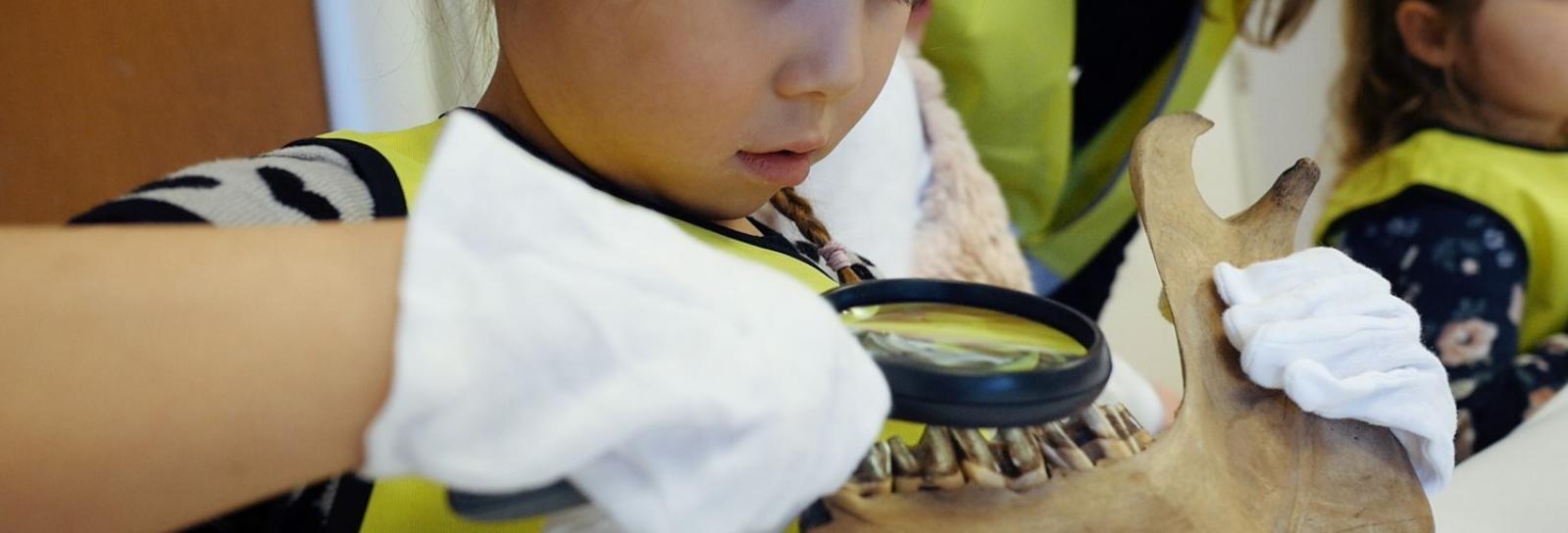 Barn undersøger arkæologisk fund med lup