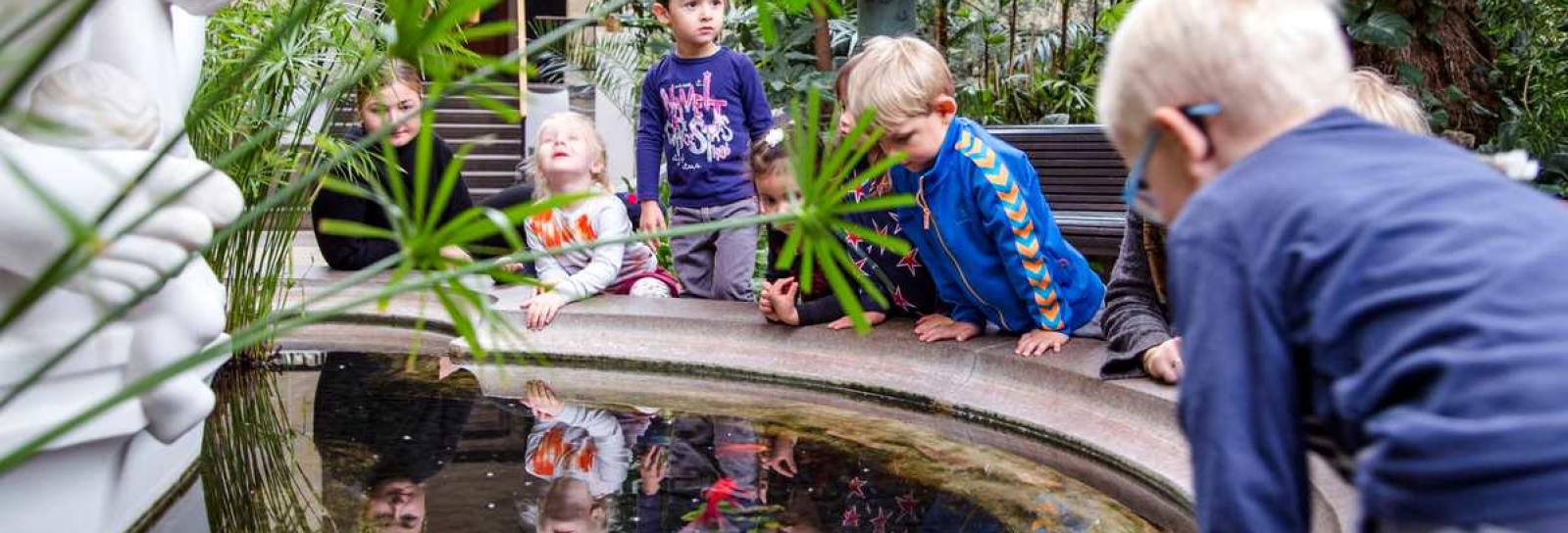 Børnehavebørn ser på guldfisk i bassinet i Glyptotekets vinterhave. 