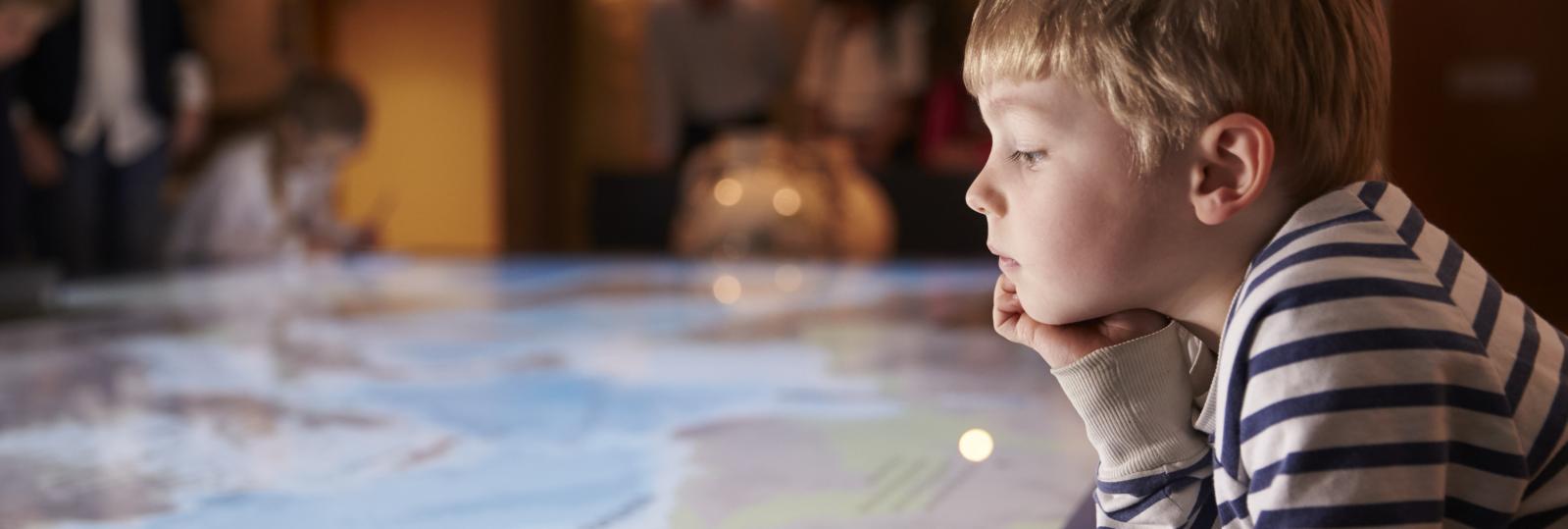 Dreng på 4-5 år med stribet trøje kigger ned på på et kort