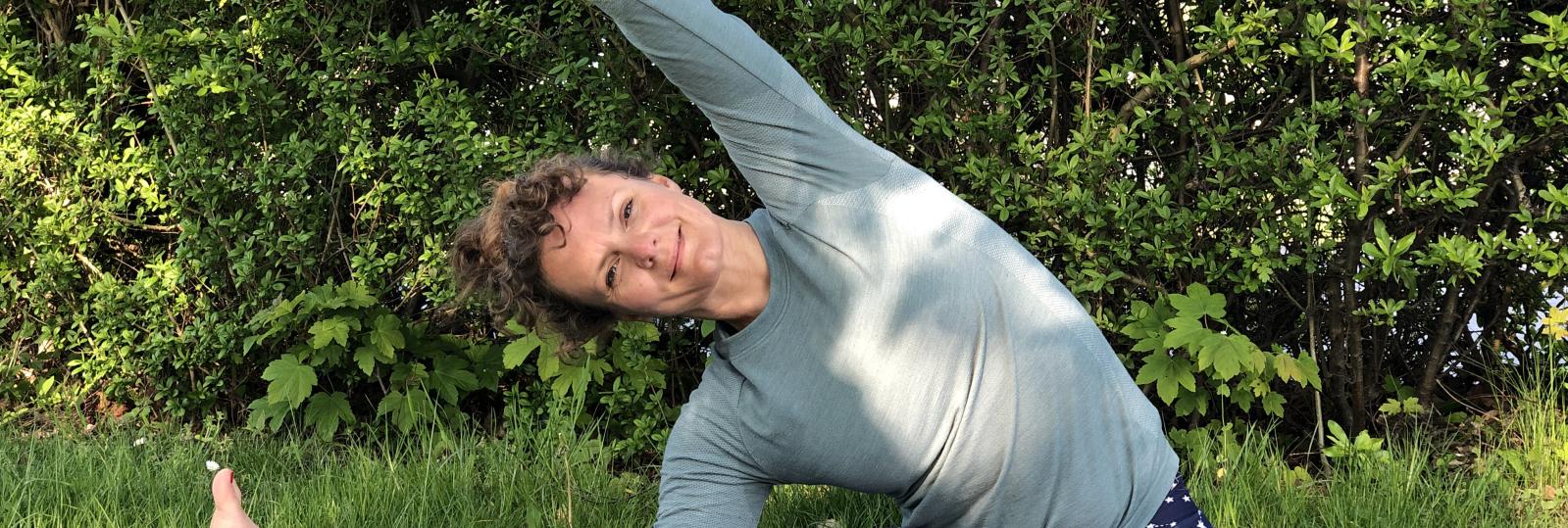 Katrine sidder udenfor i græsset, med kroppe strakt til siden over højre ben.