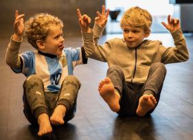 To store børnehavebørn laver siddende balanceøvelse på gulvet